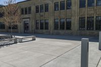 an empty courtyard with benches and tables in front of a brick building of a large, stone, factory or college building