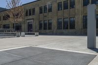 an empty courtyard with benches and tables in front of a brick building of a large, stone, factory or college building