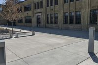 an empty courtyard with benches and tables in front of a brick building of a large, stone, factory or college building