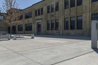 an empty courtyard with benches and tables in front of a brick building of a large, stone, factory or college building