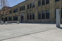 an empty courtyard with benches and tables in front of a brick building of a large, stone, factory or college building