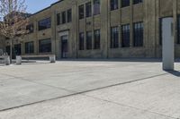 an empty courtyard with benches and tables in front of a brick building of a large, stone, factory or college building