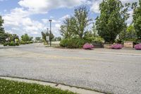 a park bench is placed at the end of the street between two trees and bushes