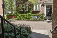 the front of a building with plants and flowers behind it with a sign that reads the city is an open house