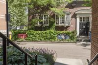 the front of a building with plants and flowers behind it with a sign that reads the city is an open house