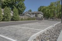 a large parking lot with some trees and rocks in the background in front of the house