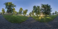 some trees and buildings in the grass on a clear day by a river, taken in a fisheye lens