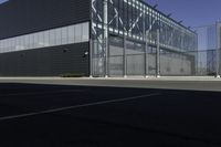 the empty parking lot of an industrial warehouse with glass doors on one side and metal bars on one side