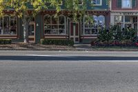 a street with green buildings and two stores on both sides of the road and trees lining the sidewalk