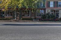 a street with green buildings and two stores on both sides of the road and trees lining the sidewalk