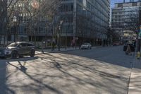 an empty city street with cars driving in the sun and people walking on the sidewalk