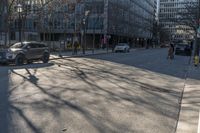 an empty city street with cars driving in the sun and people walking on the sidewalk