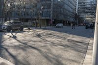 an empty city street with cars driving in the sun and people walking on the sidewalk