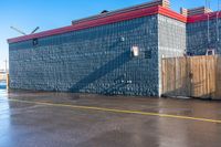 a building on the side of a road in front of an empty parking lot where people are sitting and walking in