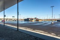 a long street near a parking lot under blue skies and snow on the ground with a sign in it