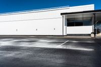 an empty lot with a large white building in the background and parking spaces on either side