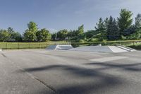 a skate park has some ramps in the area near trees and grass, as seen on this view