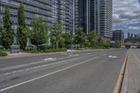 the empty street has white markings on it and is lined with trees and apartment buildings