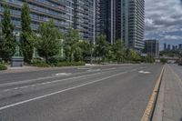 the empty street has white markings on it and is lined with trees and apartment buildings