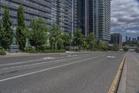 the empty street has white markings on it and is lined with trees and apartment buildings