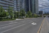 a paved road near two tall buildings in an urban setting with green trees and shrubs