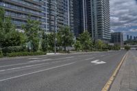 a paved road near two tall buildings in an urban setting with green trees and shrubs