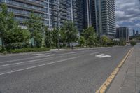 a paved road near two tall buildings in an urban setting with green trees and shrubs