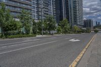 a paved road near two tall buildings in an urban setting with green trees and shrubs