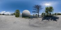 a wide angle lens of the sphere shaped building that is in a parking lot with the reflection of a lake