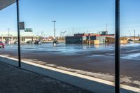 view of commercial parking lot in winter with cars parked on wet surface by sidewalk in outdoor area