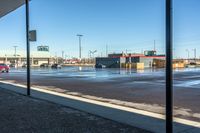 view of commercial parking lot in winter with cars parked on wet surface by sidewalk in outdoor area