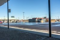 view of commercial parking lot in winter with cars parked on wet surface by sidewalk in outdoor area