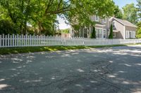 a white house with a white picketed fence on the side and grass behind it