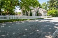 a white house with a white picketed fence on the side and grass behind it