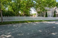 a white house with a white picketed fence on the side and grass behind it