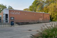 a man is walking toward a theater building from outside, looking at a sign on the side of a building with a tree