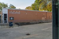 a man is walking toward a theater building from outside, looking at a sign on the side of a building with a tree