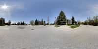 a 360 - view looking into the lens of a house in an empty street with some trees in a small neighborhood