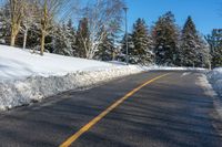 a road with some snow on it, and trees in the background with a yellow line in the middle