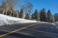 a road with some snow on it, and trees in the background with a yellow line in the middle