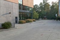 a sidewalk in front of a building next to a park with trees, bushes and people