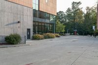 a sidewalk in front of a building next to a park with trees, bushes and people