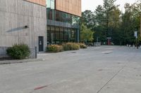 a sidewalk in front of a building next to a park with trees, bushes and people