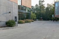 a sidewalk in front of a building next to a park with trees, bushes and people