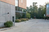 a sidewalk in front of a building next to a park with trees, bushes and people