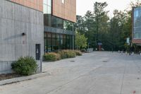 a sidewalk in front of a building next to a park with trees, bushes and people