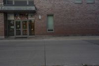 an empty fire hydrant stands in front of a brick building with no cars on it