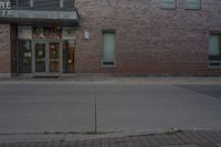 an empty fire hydrant stands in front of a brick building with no cars on it