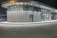 a circular building at night with traffic going by by it and people on the sidewalk