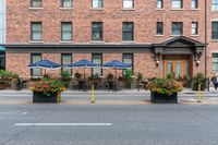 some tables with blue umbrellas and flower pots with flowers on them and yellow poles